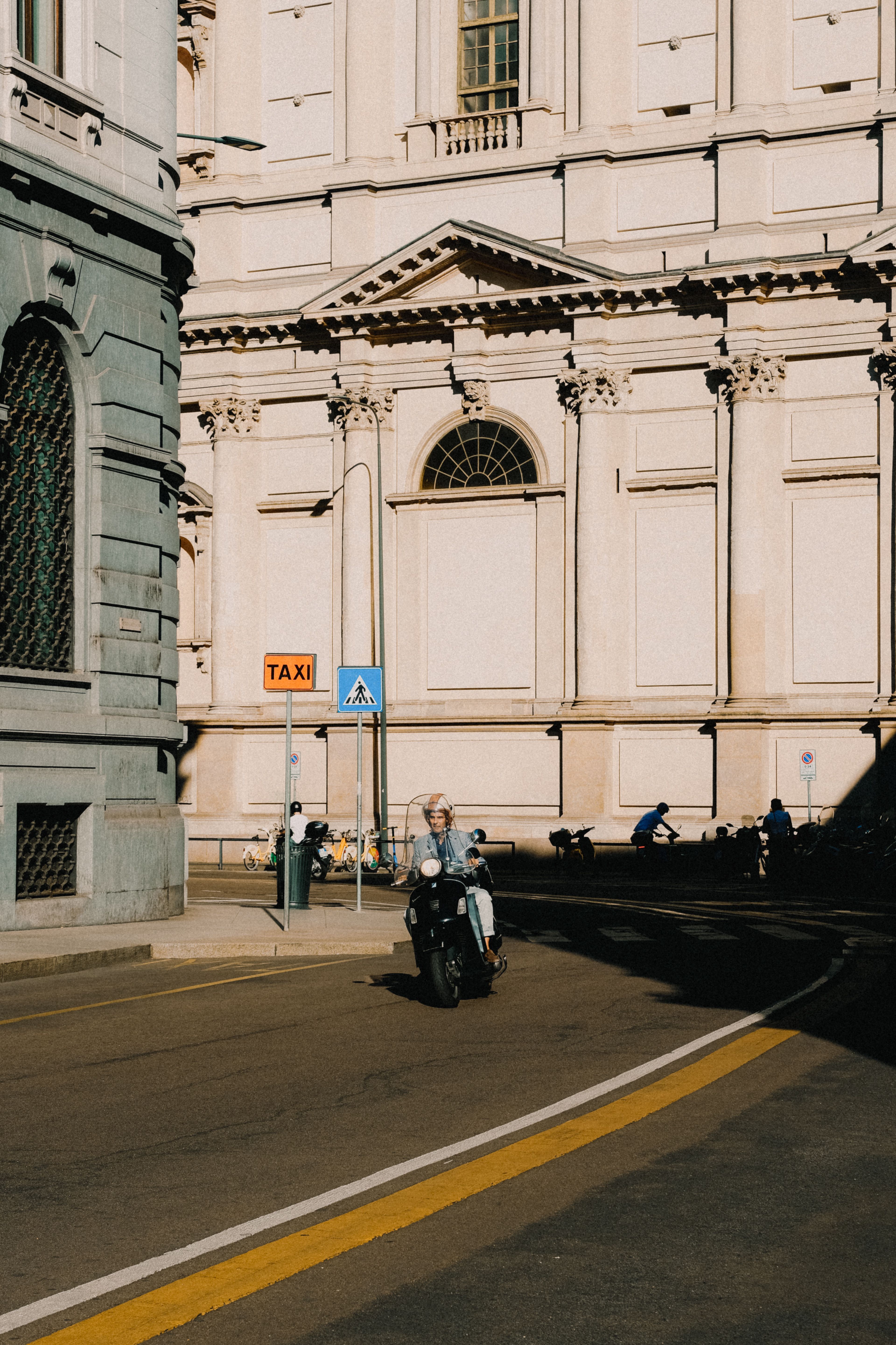 A scooter rider on a city street in front of a historic building in warm sunlight.