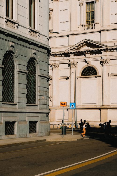 Free Sunlit historic city buildings with people walking by, capturing urban architecture and daily life. Stock Photo