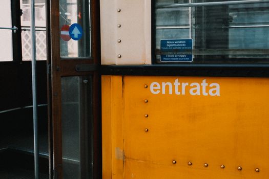 Detailed view of a yellow tram entrance with 'entrata' text and ticket warning sign.