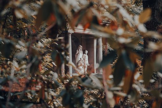 A statue seen through autumn leaves, creating a serene and contemplative scene in the park.
