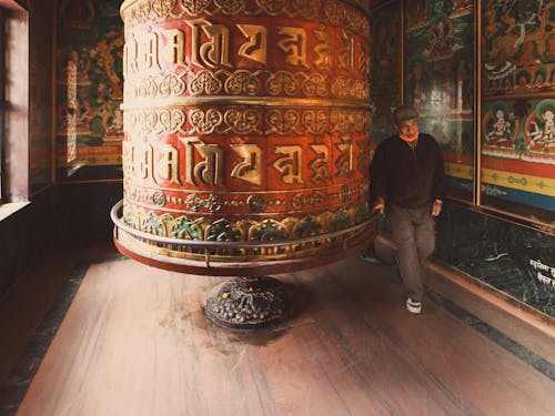 Elderly Man Standing beside a Big Prayer Wheel in the Boudhanath Temple, Nepal 