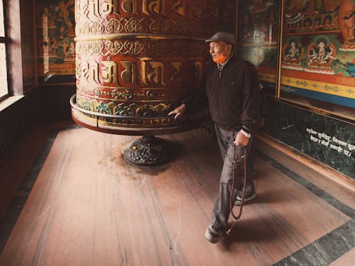 Elderly Man Standing beside a Big Prayer Wheel