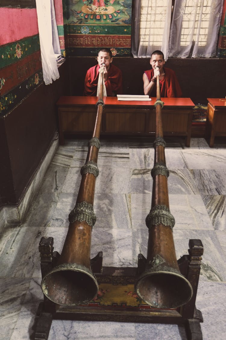 A Pair Of Man Blowing A Pair Of Brown Wooden Trumpets 