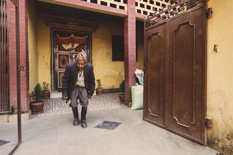 Photo Of An Elderly Asian Man Standing Next To A Gate To A Building