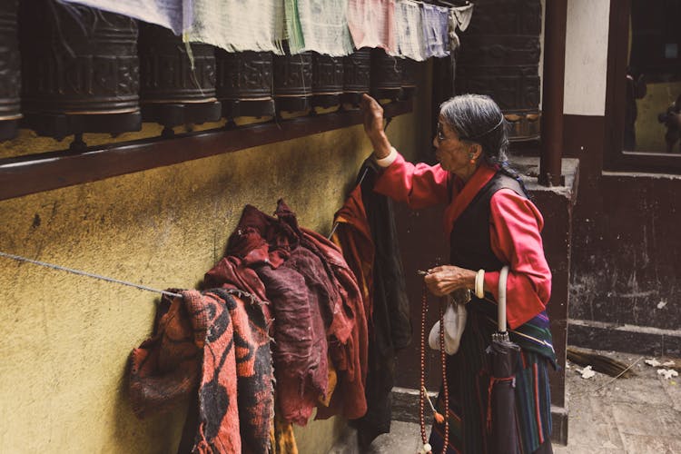 Old Woman Touching Wooden Prayer Wheels