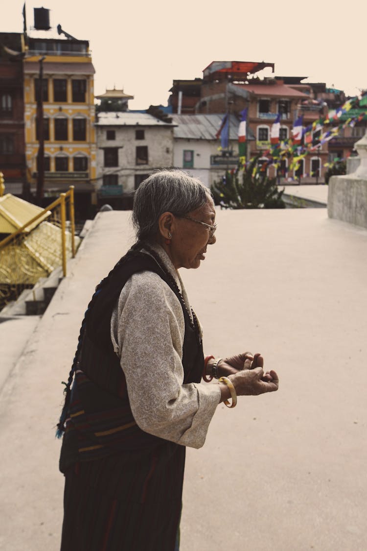 Photo Of An Elderly Person Standing In A Square Against The Background Of Buildings