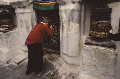 Photo of a Woman Bowing in Front of the Doors of a Buddhist Temple