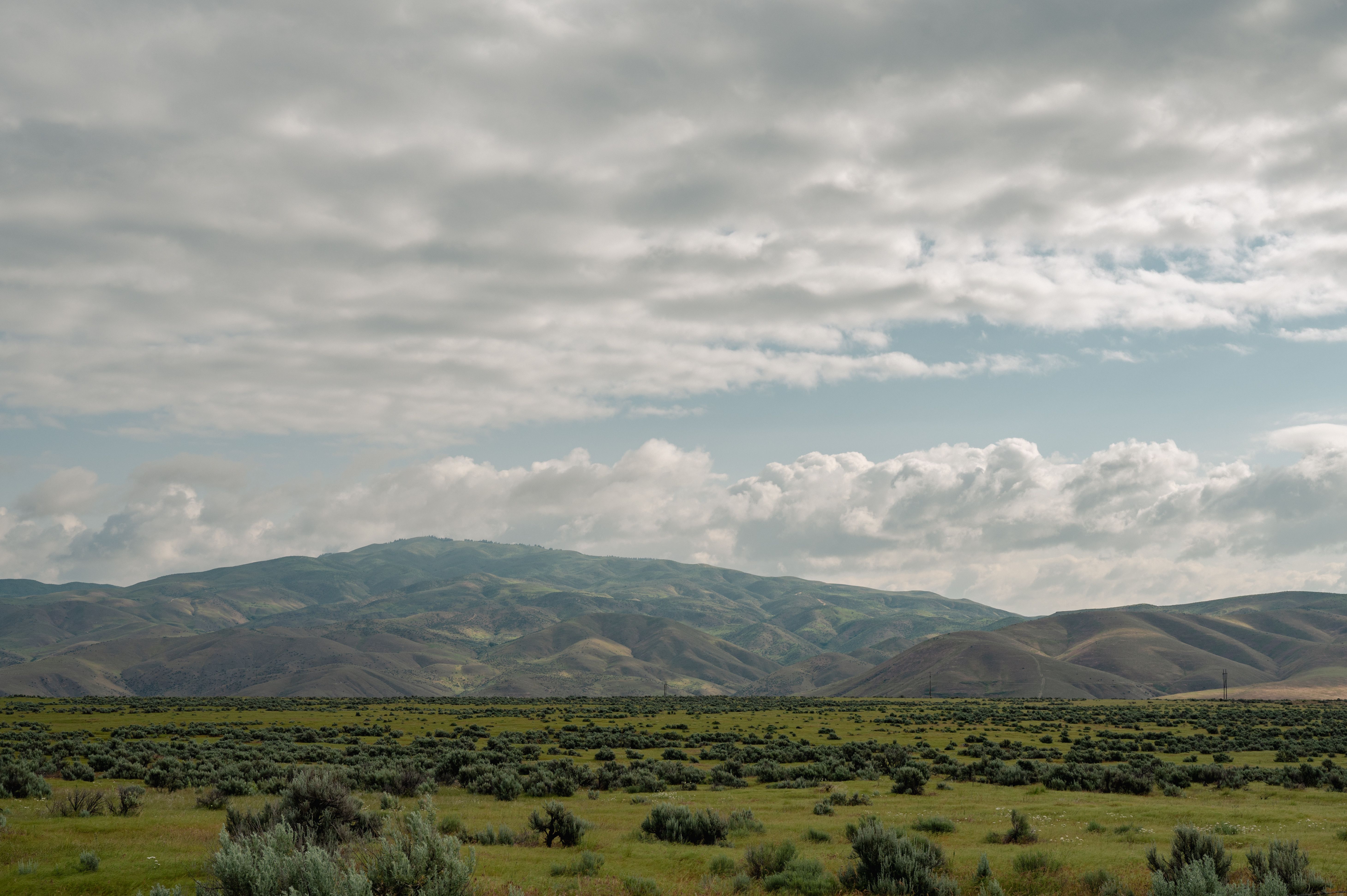 Grass Field Near Mountains Under a Cloudy Sky · Free Stock Photo
