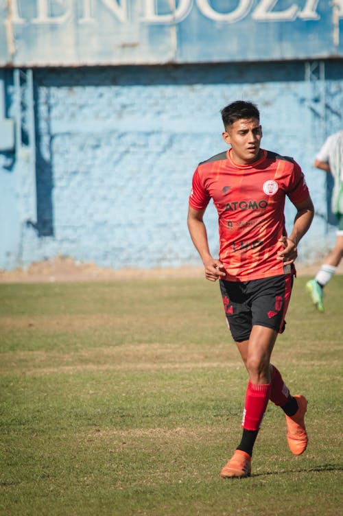 A Man Wearing a Red Jersey Shirt Running on a Grass Field