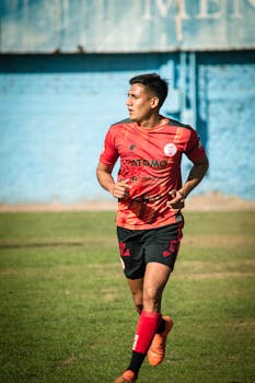 Soccer player in red uniform running on a field in Mendoza, Argentina under clear sky.