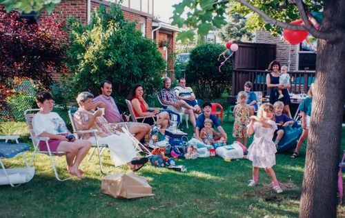 Free A joyful family gathering outdoors with children playing and adults relaxing in the backyard. Stock Photo