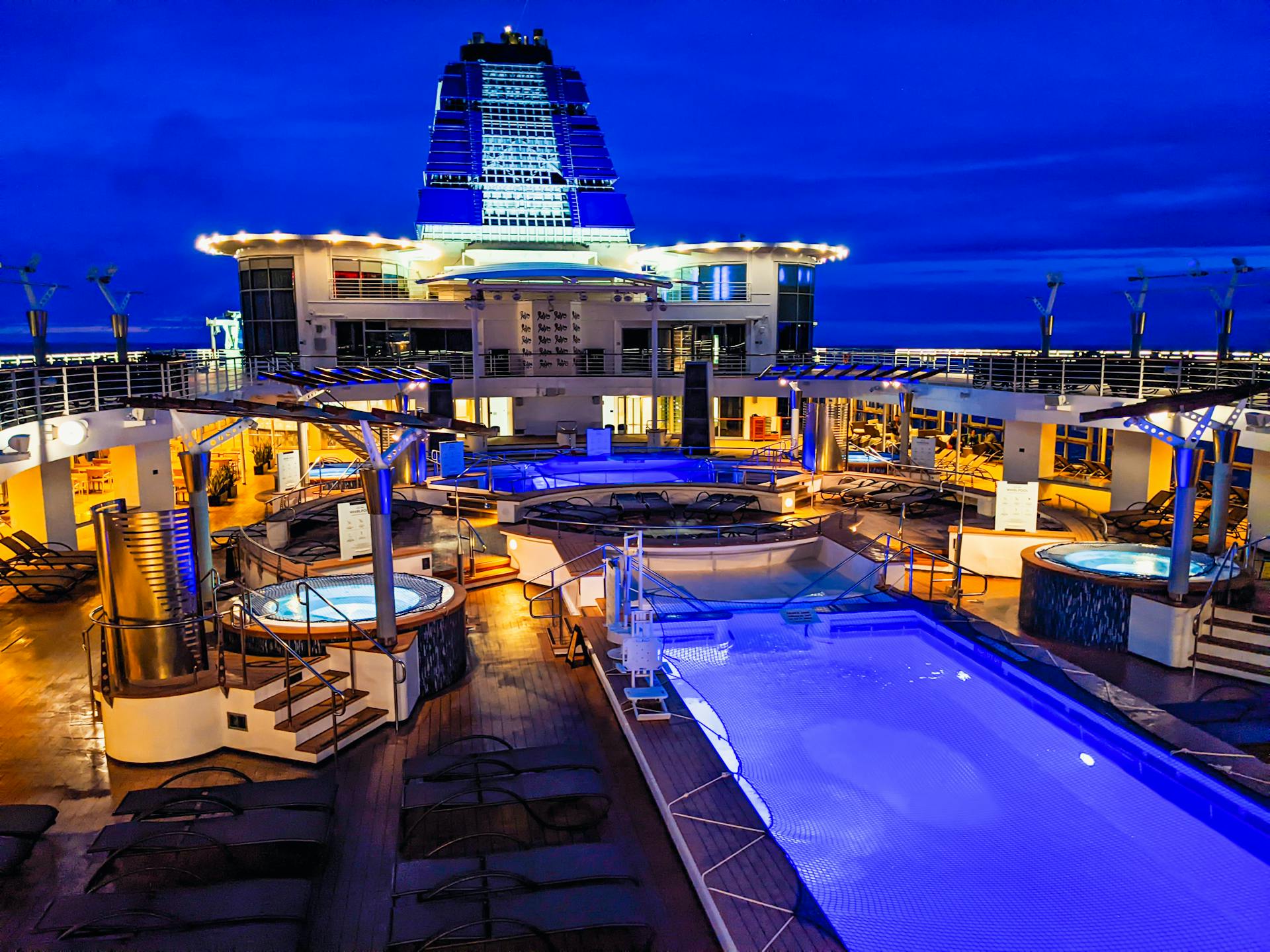 Stunning cruise ship deck featuring pools and jacuzzis under twilight skies, exuding luxury and relaxation.