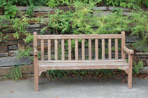 Free A rustic wooden bench set against a lush stone wall in a peaceful park. Stock Photo
