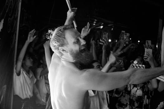 Black-and-white photo of a lively shirtless performer on stage with an enthusiastic crowd.