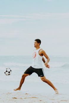 A young man plays soccer on the sandy beach of Canoa Quebrada, Brazil, enjoying a sunny day by the sea.