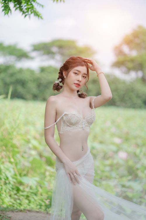Free A beautiful woman poses outdoors in delicate attire, illuminated by soft, dreamy lighting. Stock Photo