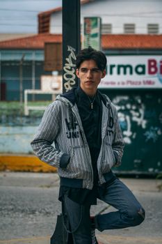 Portrait of a young man in a casual jacket leaning against a post in an urban area of Venezuela.
