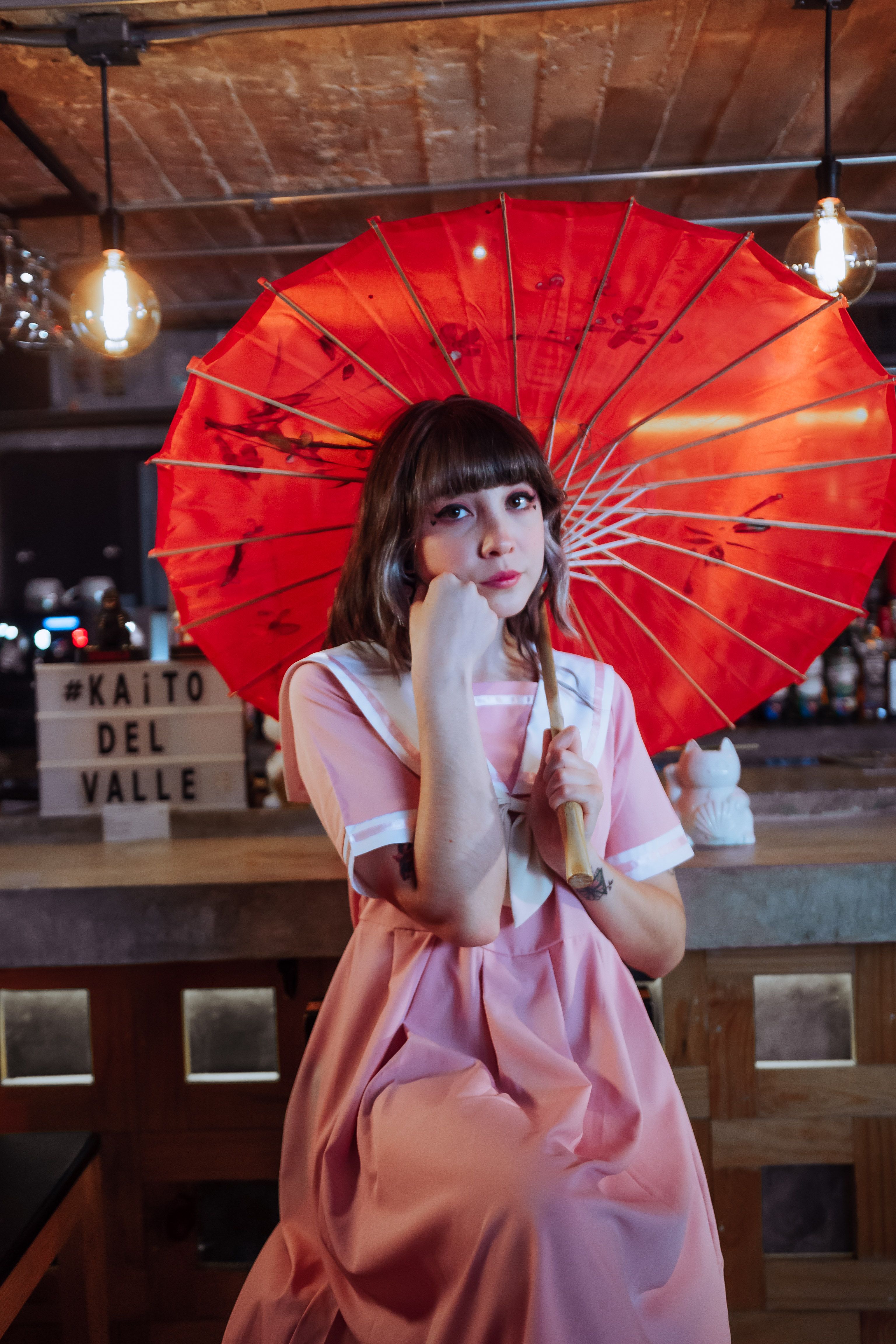 A woman in a pink dress holds a vibrant red umbrella inside a cozy café in Mexico City.