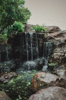A tranquil waterfall cascading over rocks surrounded by lush greenery and plants.