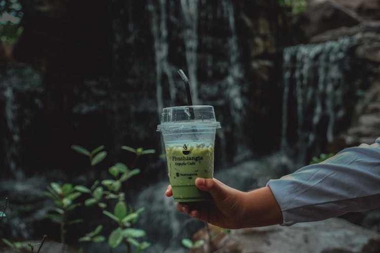 Hand Holding A Clear Plastic Cup With Green Liquid