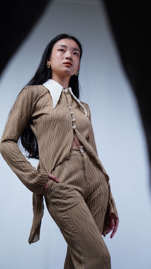 Free Stylish Asian woman in a pleated suit posing confidently against a studio backdrop. Stock Photo