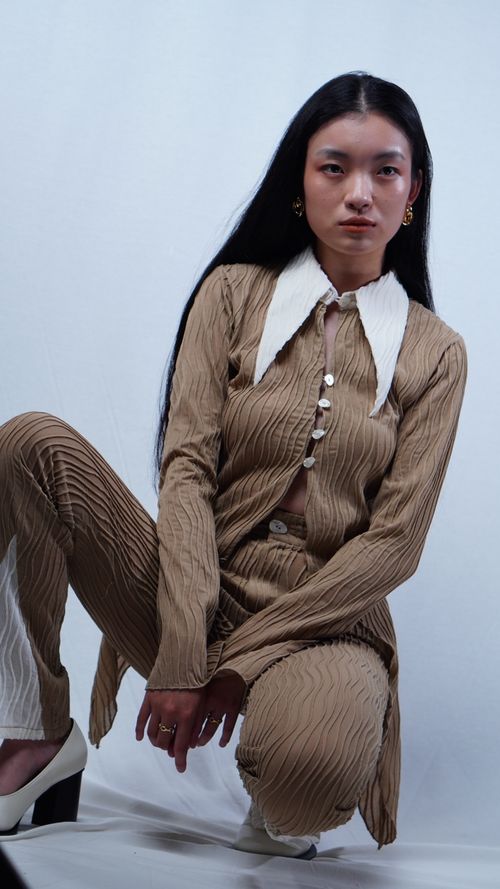 Free Portrait of a fashionable woman in a brown outfit with a striking white collar, posing indoors. Stock Photo