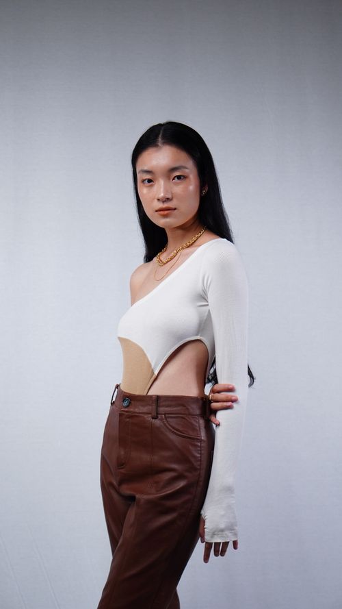 Free Asian woman wearing stylish off-shoulder top and leather pants in studio setting. Stock Photo