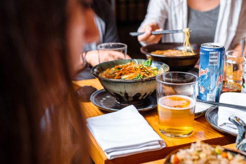 Free A vibrant dining scene featuring Asian noodle dishes, drinks, and social interaction. Stock Photo