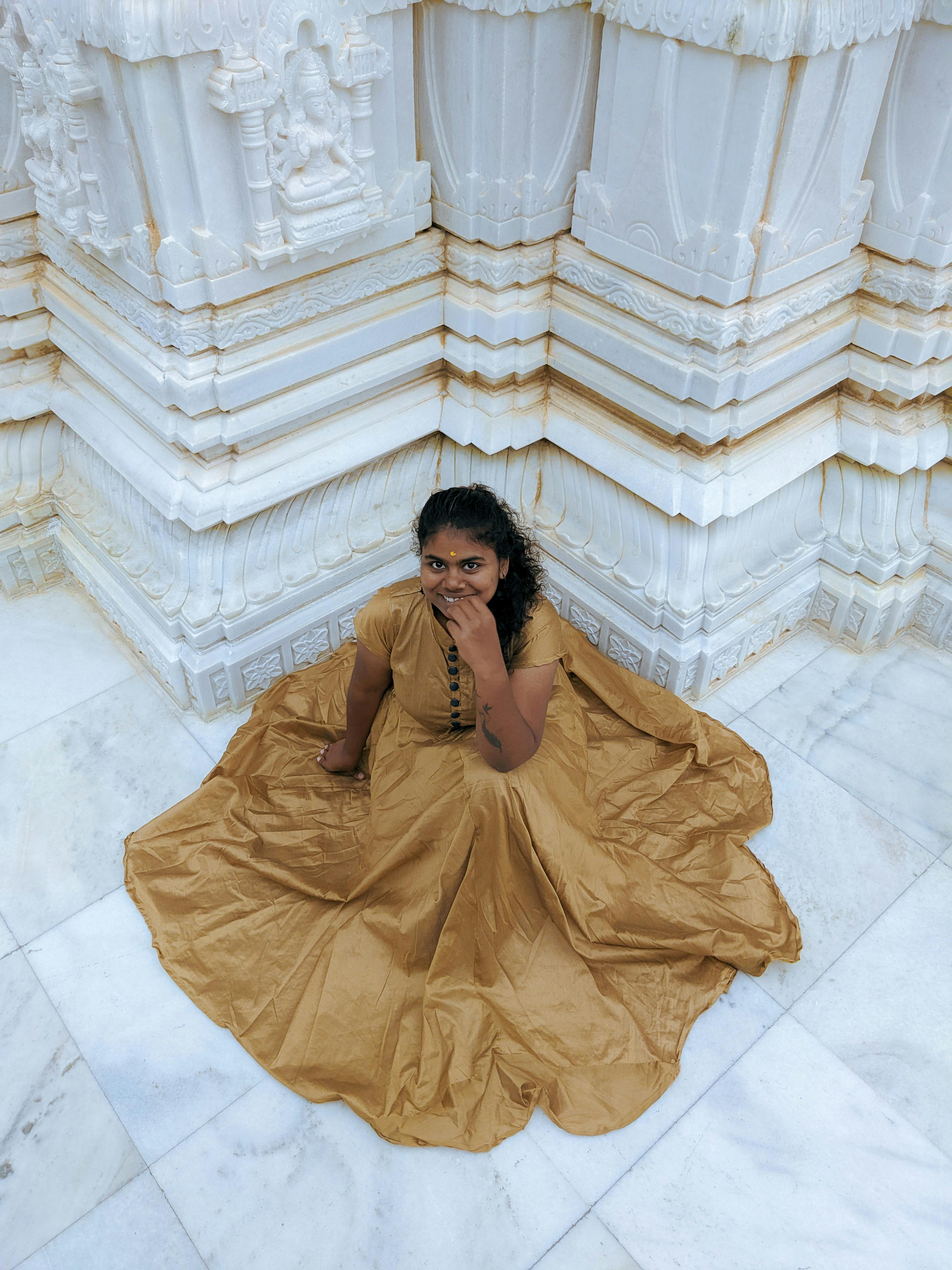 Free A woman wearing a traditional dress sits on a marble floor corner of a white ornate building, smiling. Stock Photo