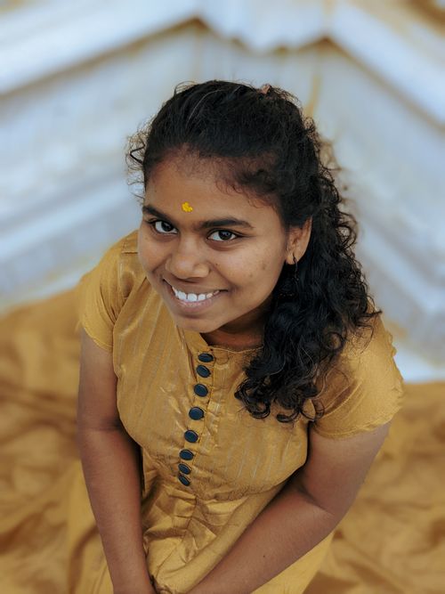 Free Smiling woman with curly hair in a mustard dress, sitting indoors with warm lighting. Stock Photo