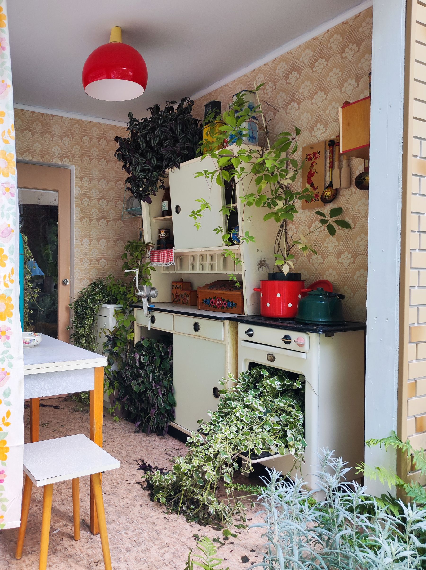 Kitchen with cream cabinets, patterned wallpaper, plants and repeated red accents