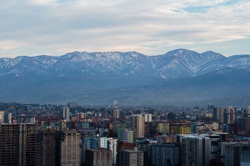 Free Cityscape view with buildings and snow-capped mountains under a cloudy sky. Stock Photo