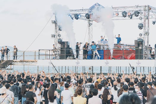 A lively crowd enjoys a DJ performance at an outdoor concert by the sea, with vibrant energy and stage effects.