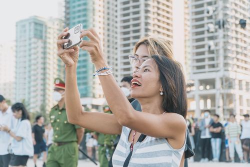 Free An Asian woman joyfully takes a photo outdoors in a bustling urban setting. Captures a lively atmosphere. Stock Photo