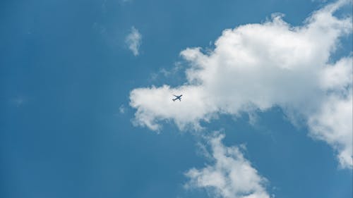 A White Airplane Flying Under White Clouds on Blue Sky
