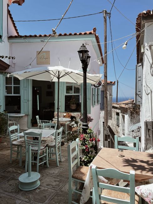 A picturesque café with teal chairs in a quaint street of Vourliotes, Greece.