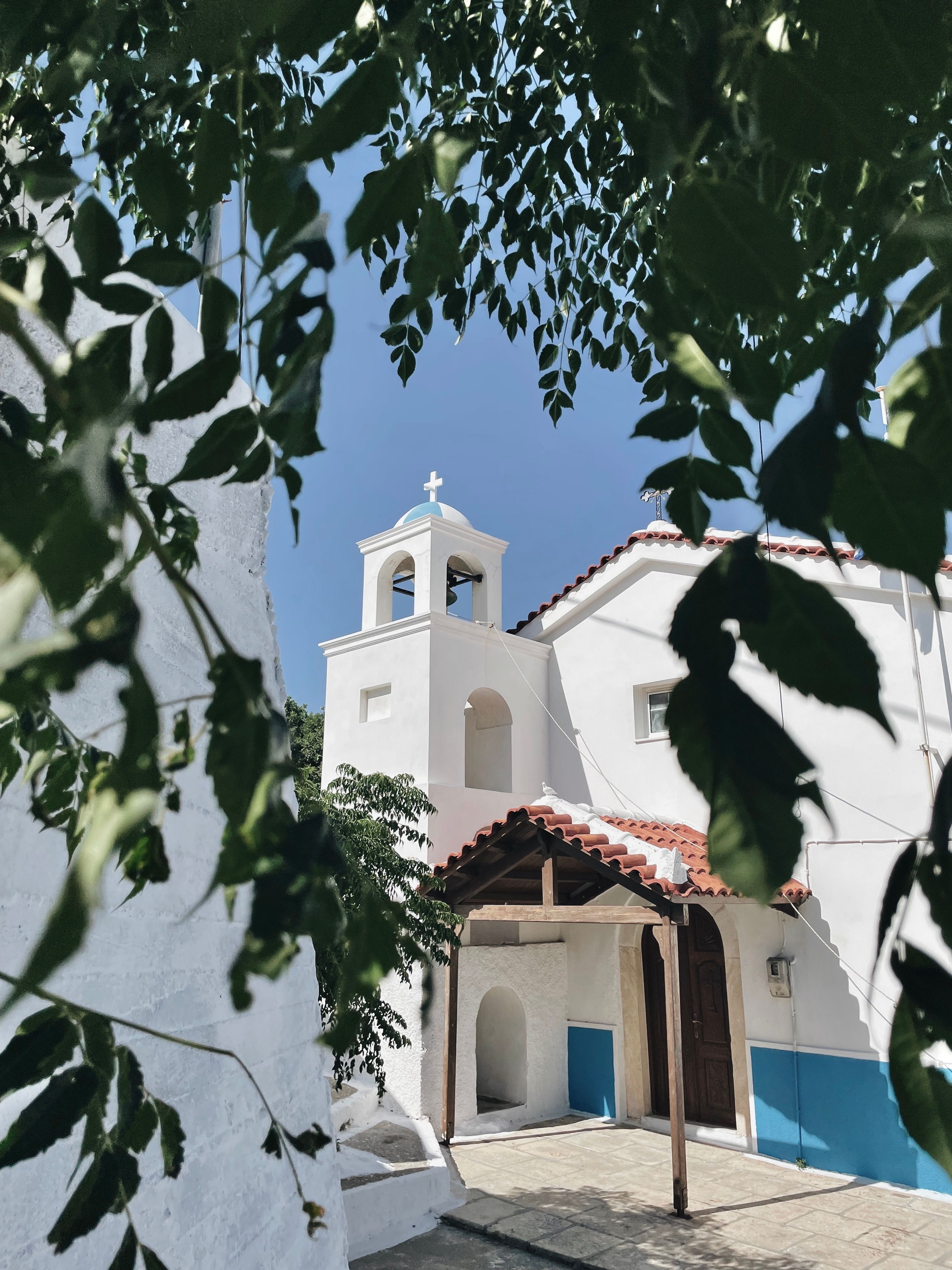 Picturesque white Greek church framed by leaves on a sunny day in Avlakia.