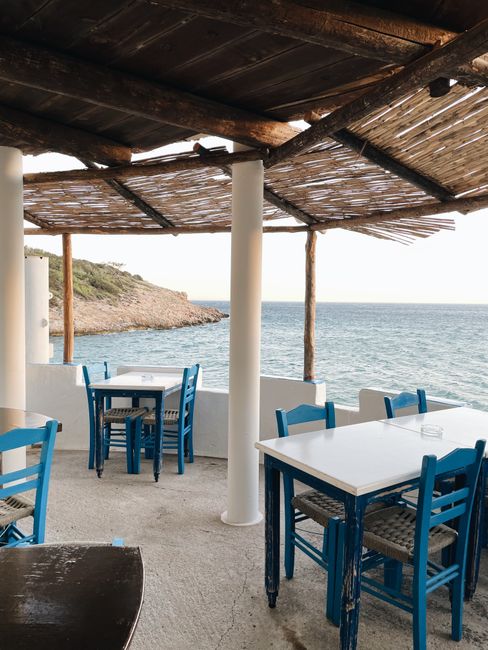 Charming seaside cafe with blue chairs offering a view of the Mediterranean coastline.