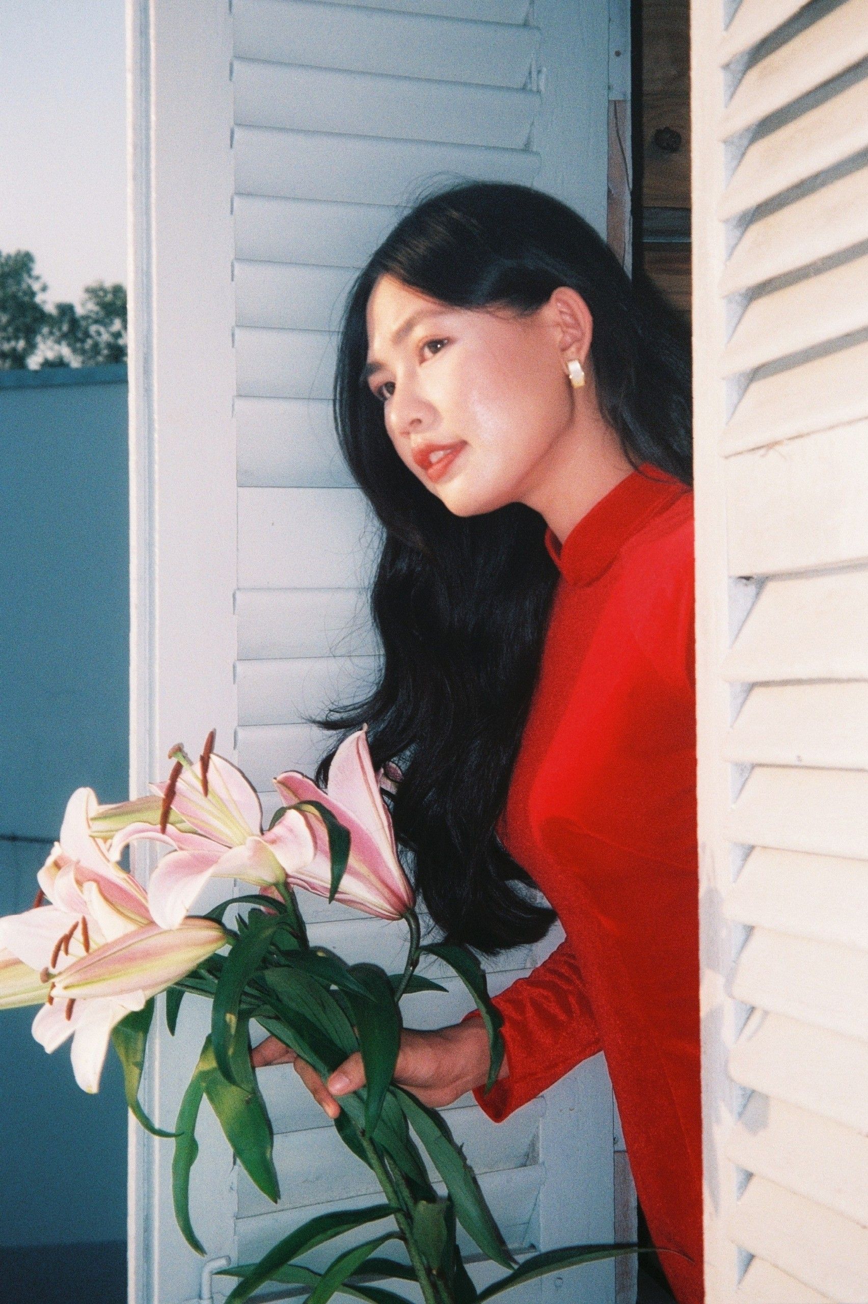 Beautiful Asian woman in red ao dai holding stargazer lilies, An Giang, Vietnam.