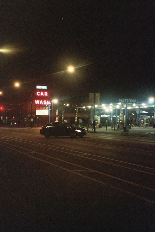 Free A black car passing by a gasoline station at night in Chicago, IL, illuminated by street lights. Stock Photo