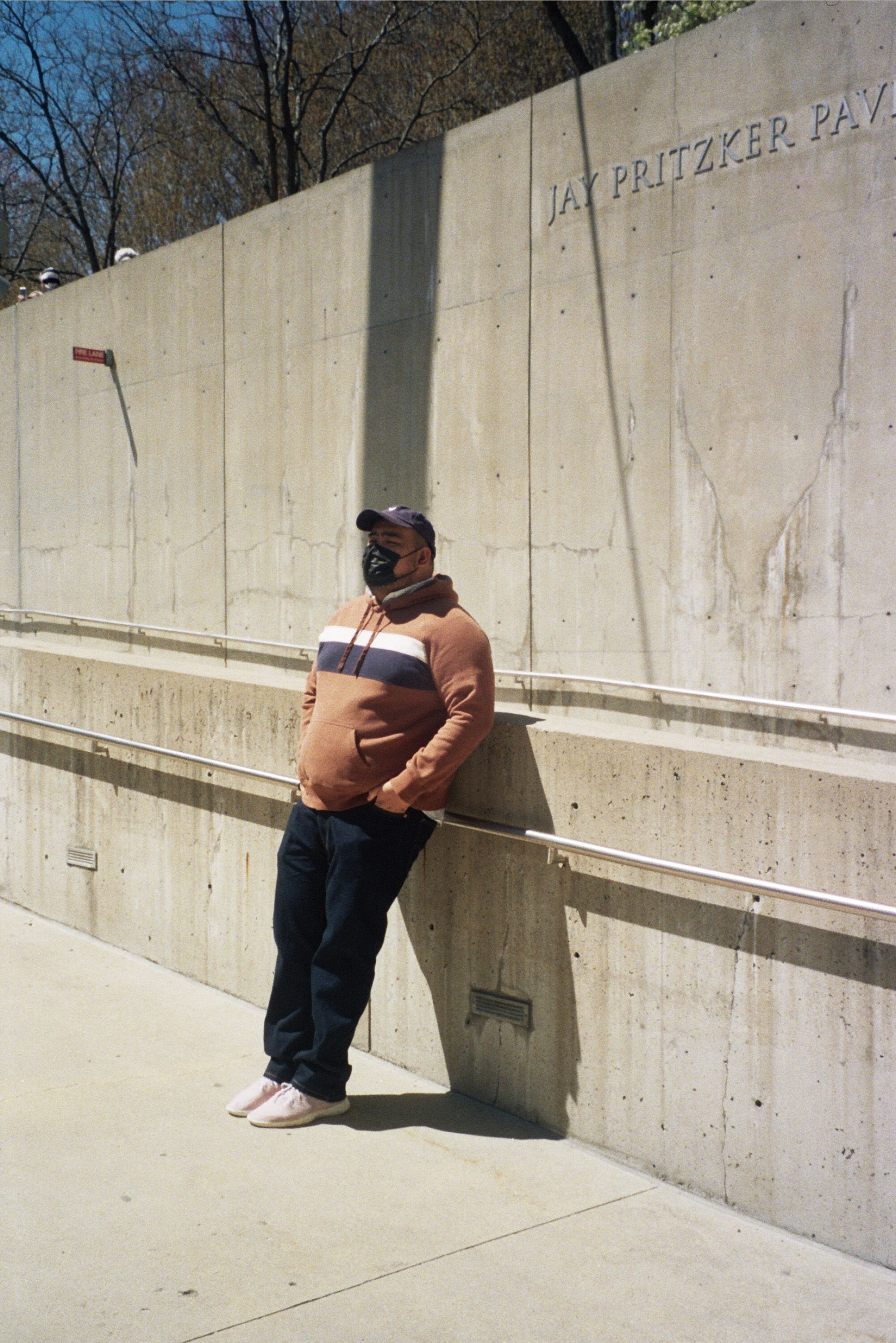 Man leaning against concrete wall at Jay Pritzker Pavilion on a sunny day.