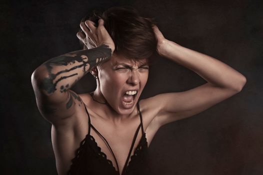 Intense studio portrait of a woman with tattoos expressing frustration.