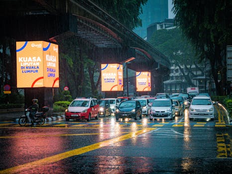 Traffic in Kuala Lumpur under heavy rain with illuminated advertisements and wet streets.