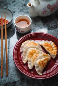 Close-up of homemade fried gyoza served with tea, showcasing vibrant Asian cuisine.
