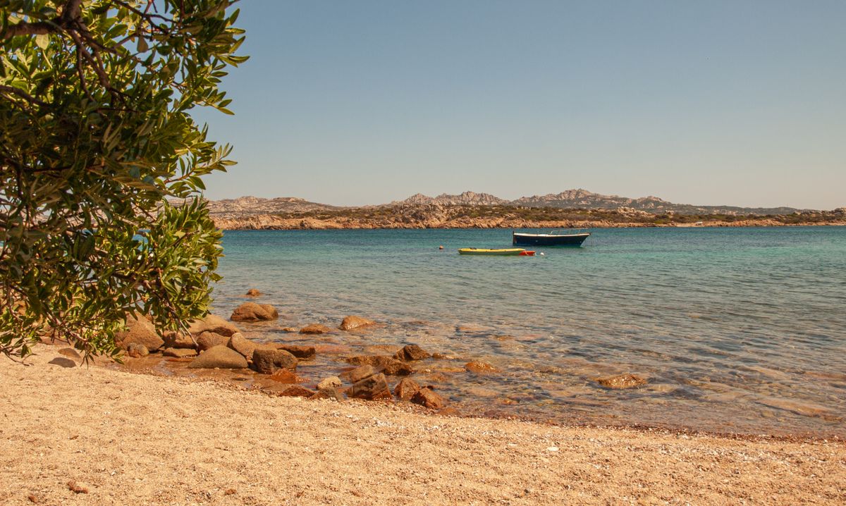 Plaja cu pietris si o barcuta verde-albastra ancorata