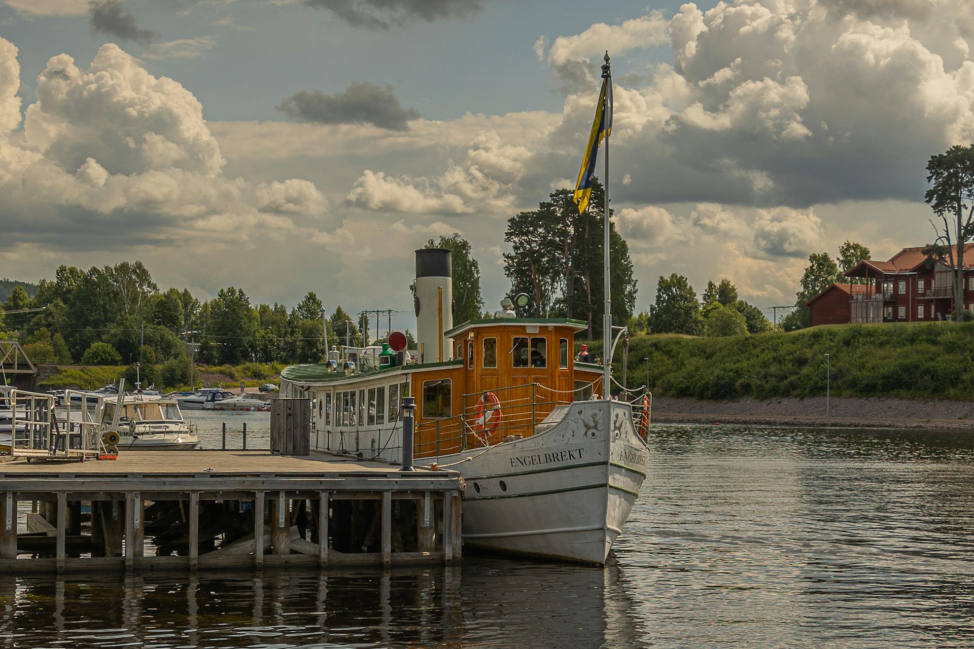 A vintage boat docked in a scenic harbor, surrounded by lush greenery and cloudy skies.