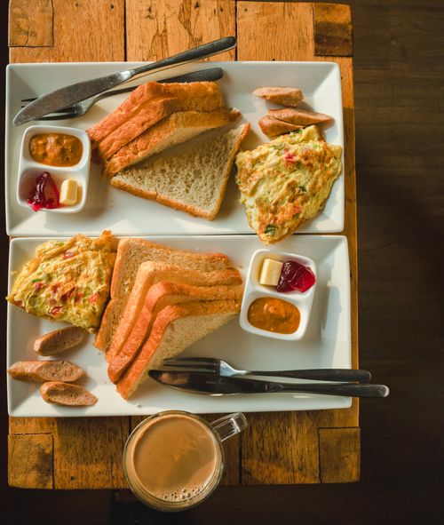Free Top view of a hearty breakfast with bread, omelette, sausages, and condiments served on a wooden table. Stock Photo