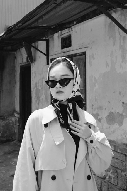 Stylish woman wearing a headscarf and coat in a vintage monochrome setting.