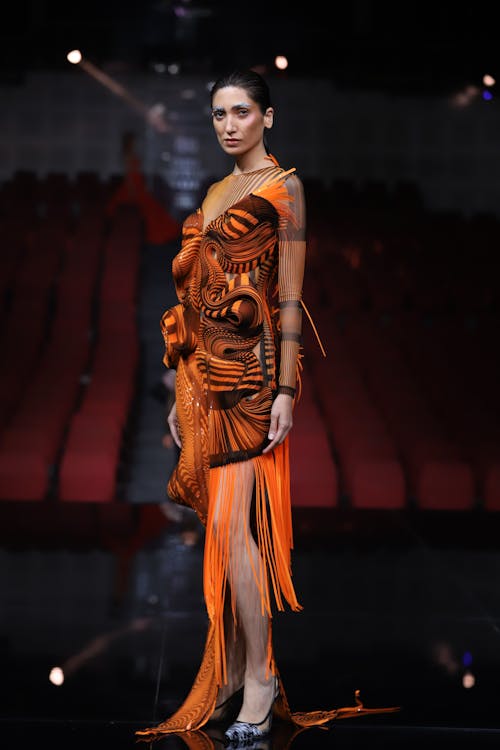 Model in Orange Dress Standing on Catwalk