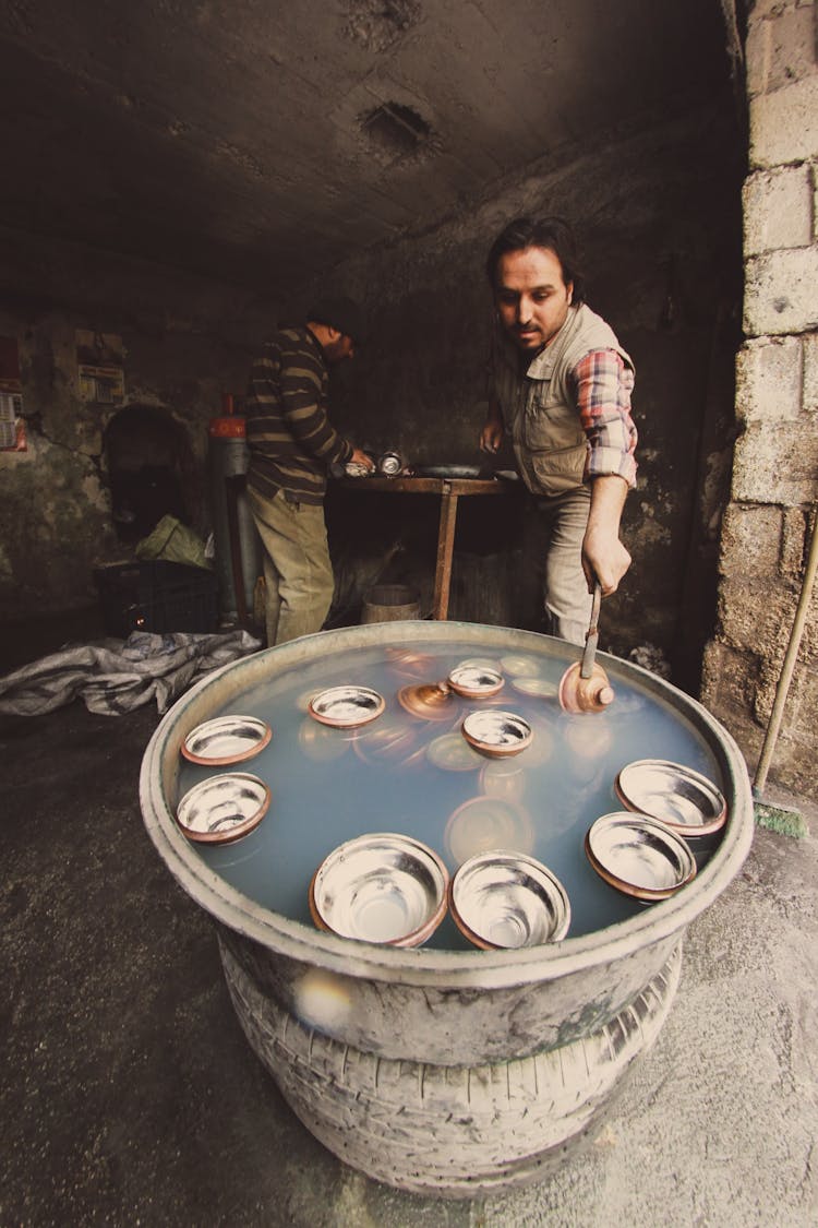 Two Men Taking Dishes Out Of A Barrel Filled With Water